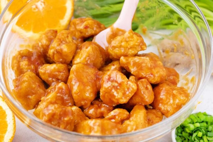 Coated fried chicken bites in orange sauce.