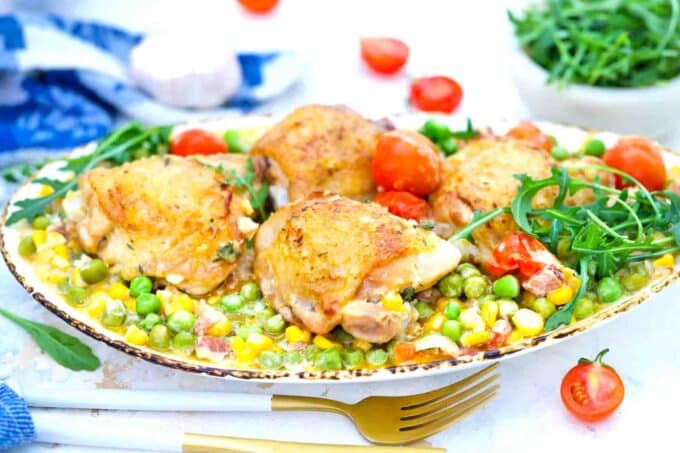 close shot of creamy corn chicken thighs on a serving plate garnished with rucola