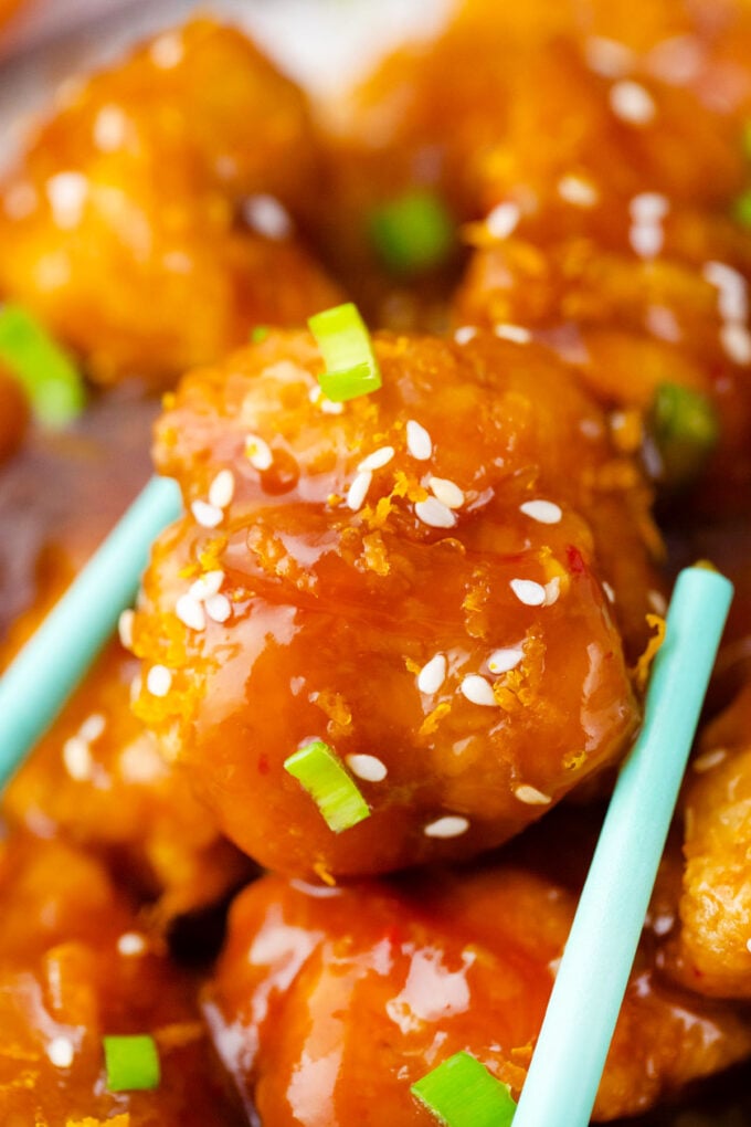 Chopsticks holding crispy orange chicken bite.
