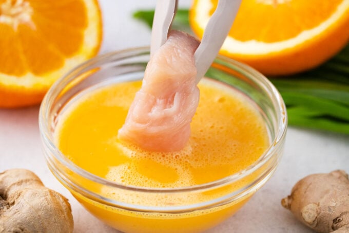 Dipping chicken piece in beaten eggs.