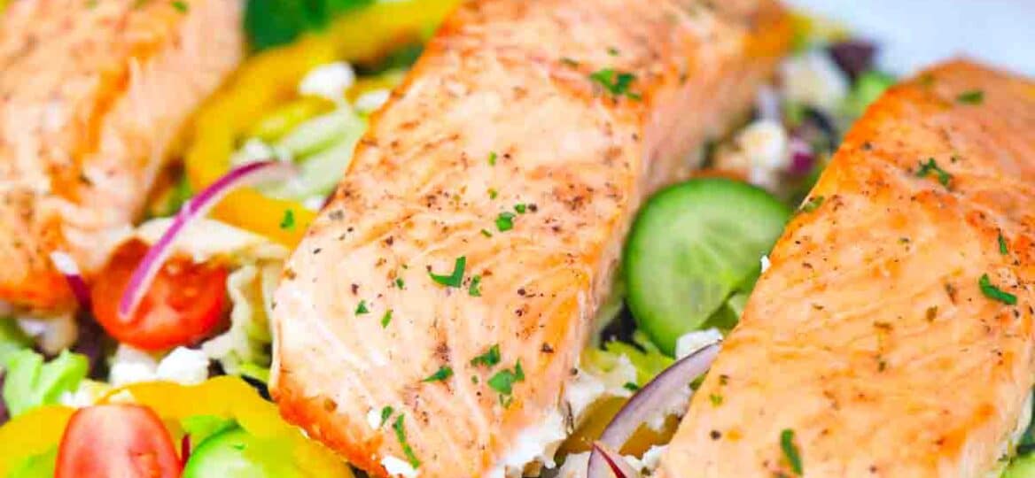 greek salmon salad on a plate topped with perfectly cooked salmon filets