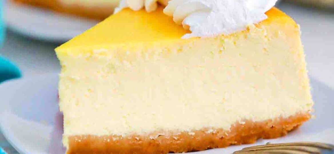 close shot of a slice of lemon ricotta cheesecake topped with whipped cream