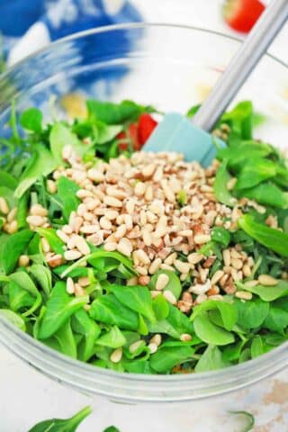 adding pine nuts to a bowl with arugula