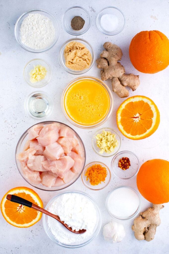 Overhead shot of Chinese orange chicken ingredients in bowls on a white surface.