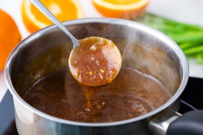 Orange sauce dripping of a spoon into a sauce pan.