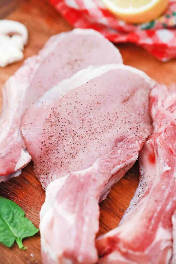 Raw bone-in pork chops on a cutting board.