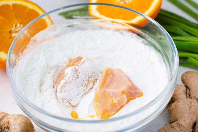 Tossing chicken pieces in a cornstarch and flour mixture.