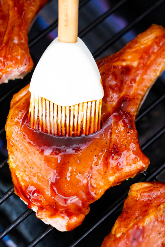 Brushing a pork chop on the grill with BBQ chili glaze.