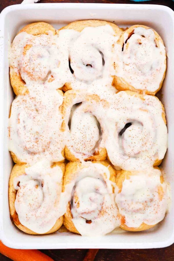 overhead shot of a baking dish with carrot cake cinnamon rolls topped with cream cheese frosting
