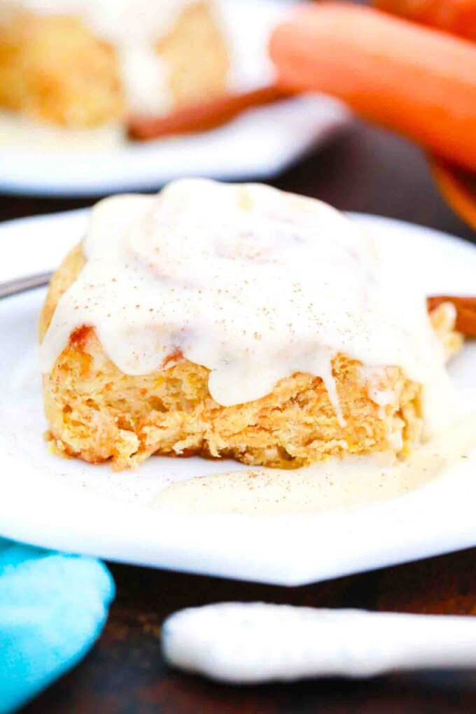carrot cake cinnamon rolls on a plate with fresh carrots in the background