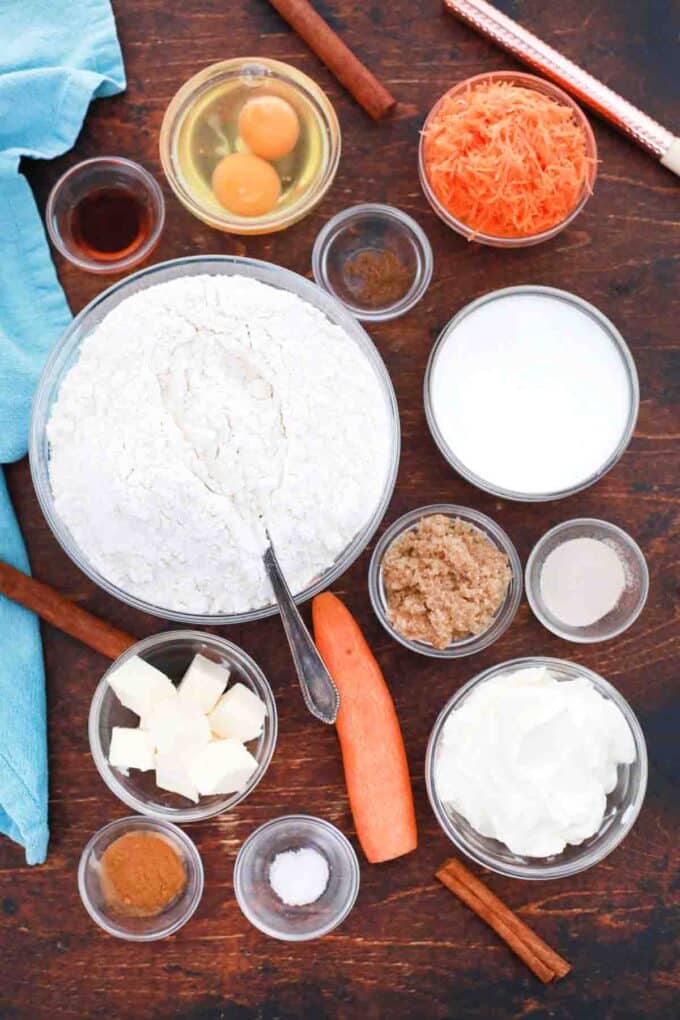 overhead shot of flour sugar carrots eggs milk spices butter raisins in bowls on table