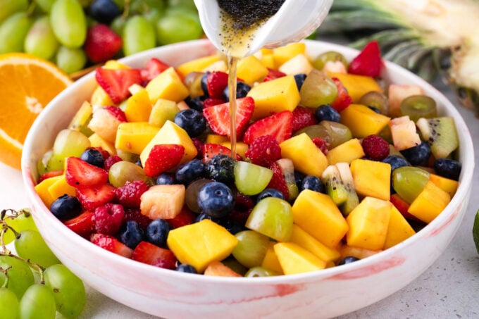 Pouring honey lime dressing over fruit salad.
