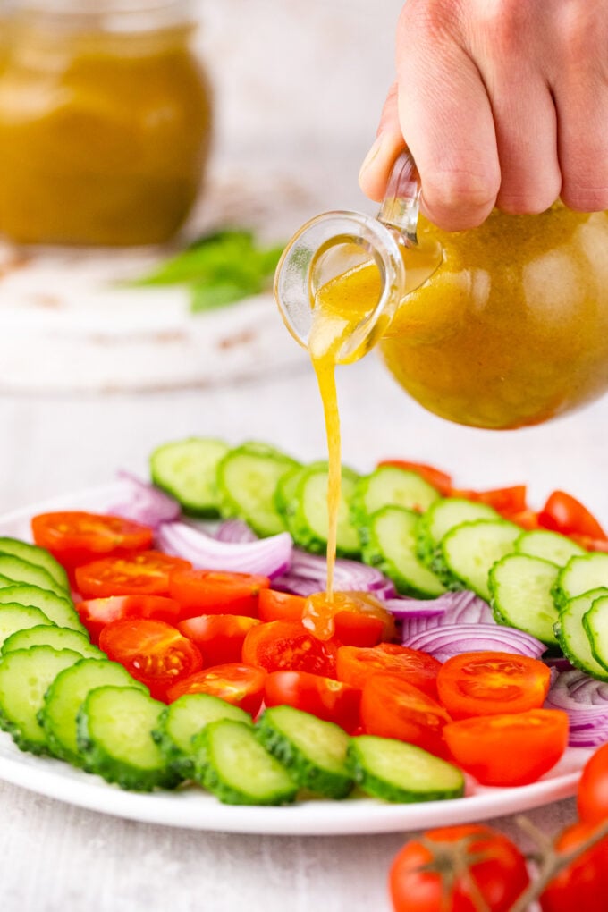 Pouring Greek salad dressing over a salad.