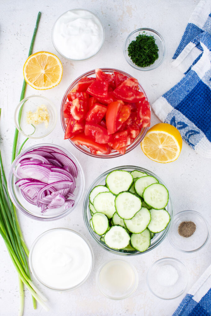 Overhead shot of creamy cucumber tomato salad ingredients in bowls.