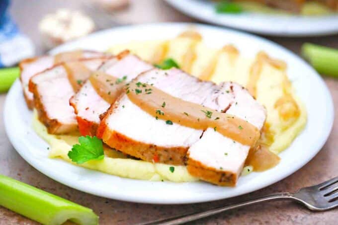 sliced crispy pork roast with gravy served with mashed potatoes