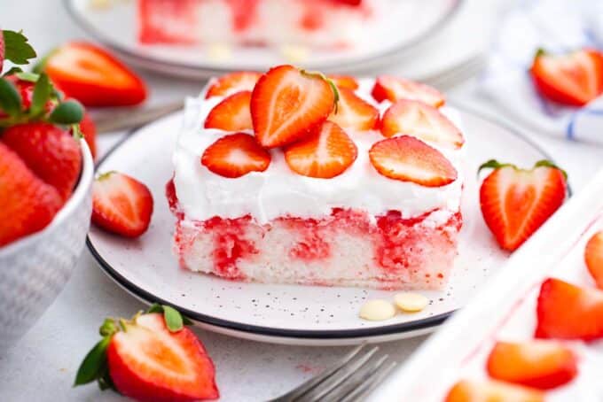 a slice of homemade strawberry poke cake topped with whipped cream and strawberries