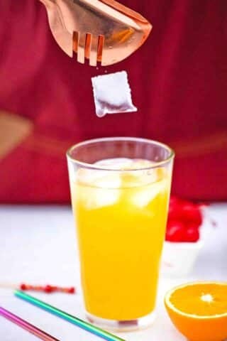 adding ice to a glass with orange juice and tequila