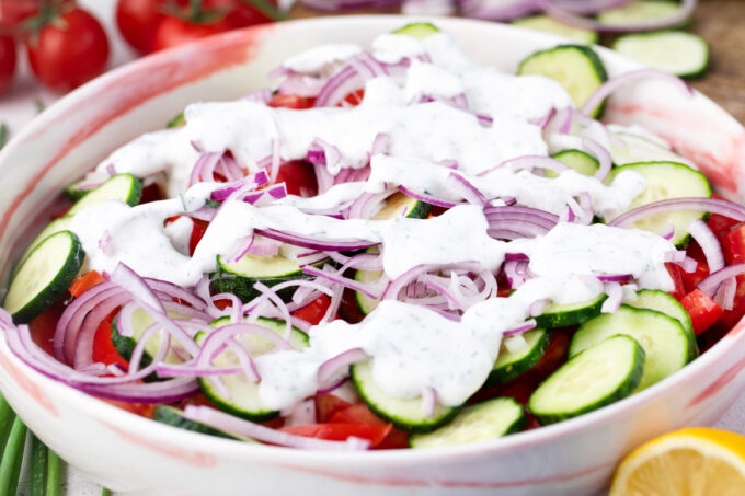 Adding creamy dressing to cucumber and tomato salad.