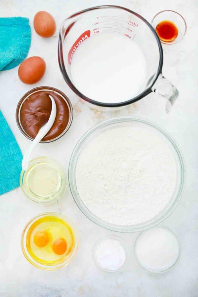 overhead shot of flour milk sugar eggs vanilla Nutella in bowls on a table
