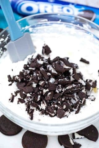 adding crushed Oreos to a mix of cream cheese and whipped cream