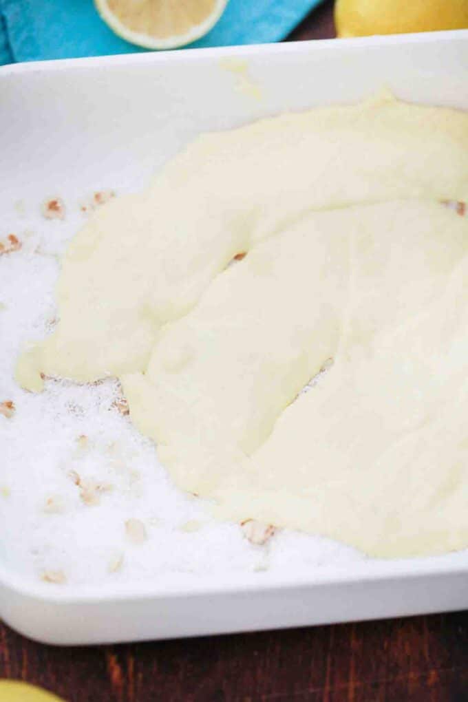 adding lemon cake batter on top of coconut flakes and nuts