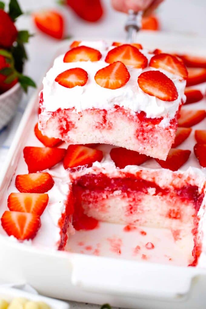 lifting a strawberry poke cake slice from the pan on a cake server