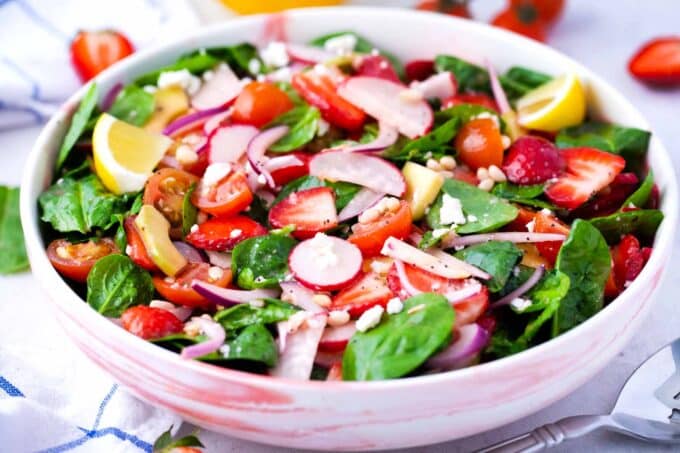 a bowl of strawberry spinach salad with red onion radishes avocado pine nuts