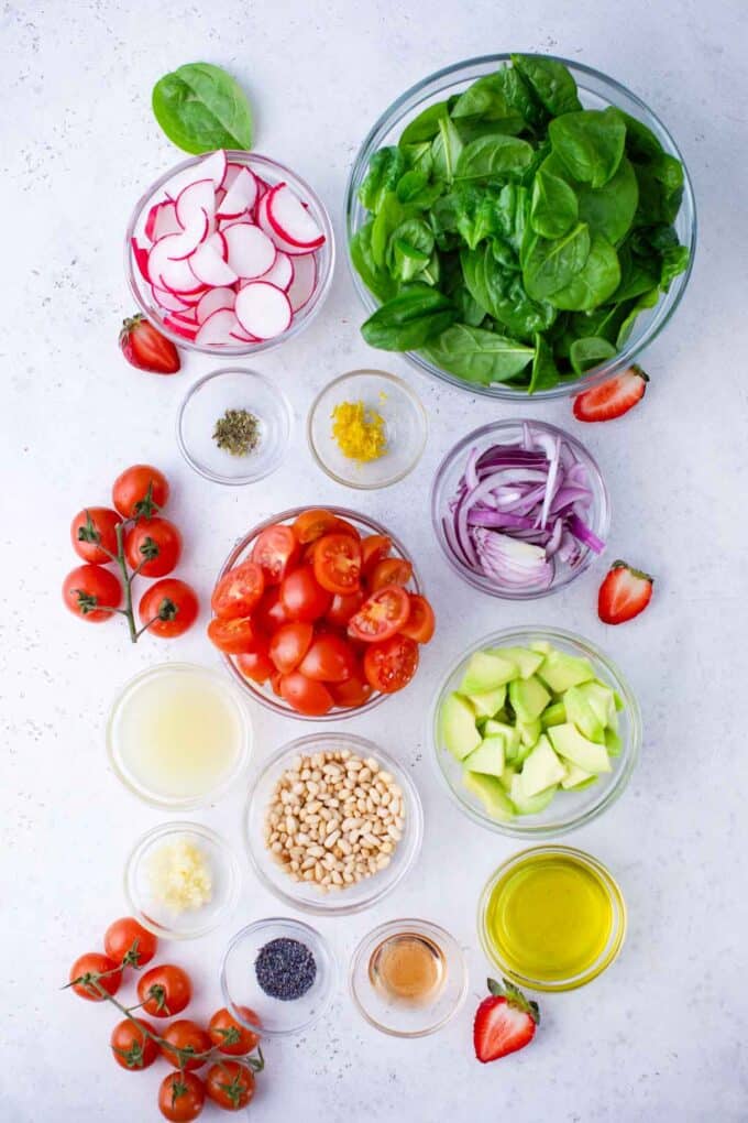overhead shot of strawberry spinach salad ingredients in bowls on a white surface