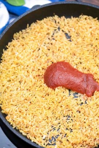 adding tomato paste to a pan of cooked orzo