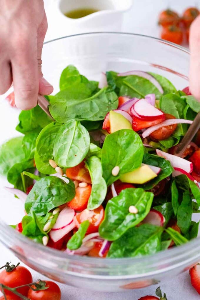 tossing strawberry spinach salad in a bowl
