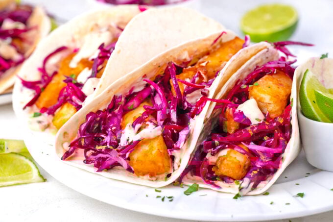 A plate of crispy Baja fish tacos with beer-battered fish, crunchy slaw, and Chipotle sauce.