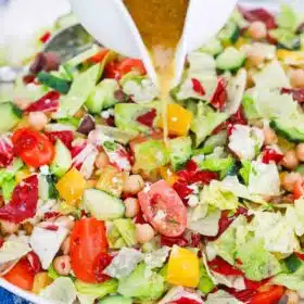 pouring dressing on top of chopped mediterranean salad