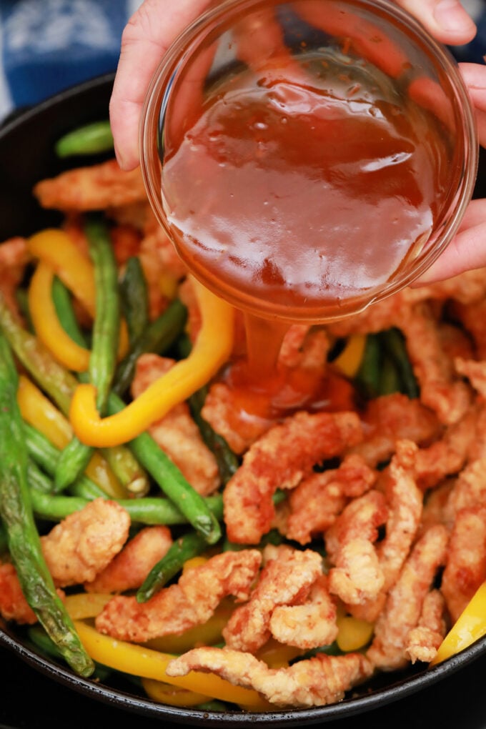 Adding honey sesame sauce to fried chicken strips with green beans and bell pepper.
