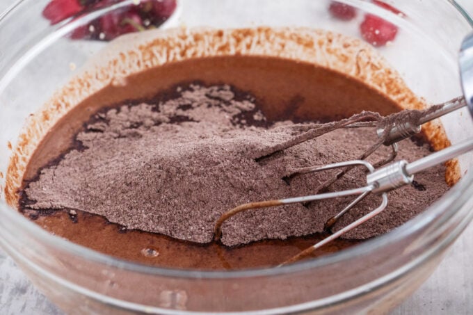 Mixing dry ingredients into wet ingredients to make chocolate cake layer.