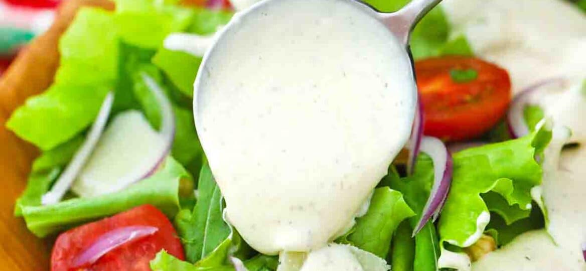 pouring creamy parmesan dressing over a salad