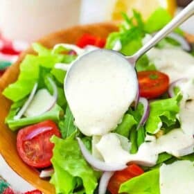 pouring creamy parmesan dressing over a salad