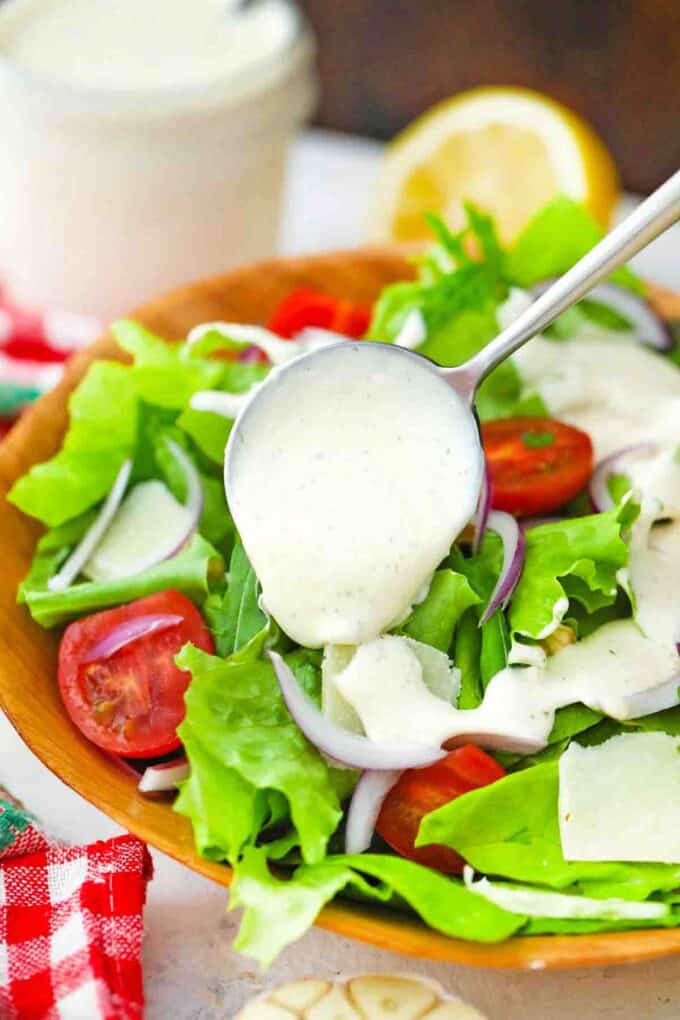 pouring creamy parmesan dressing over a salad