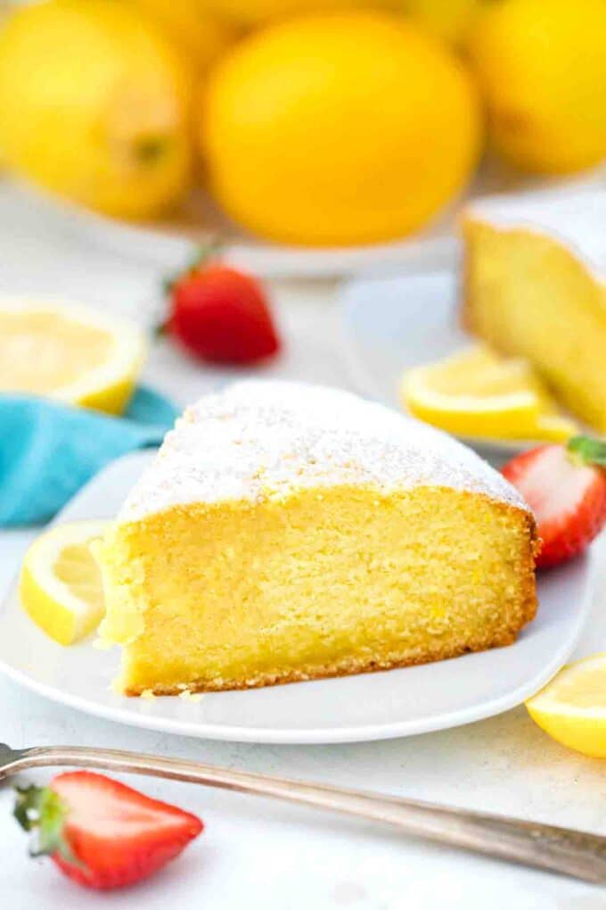 a slice of lemon ricotta cake with lemons in the background