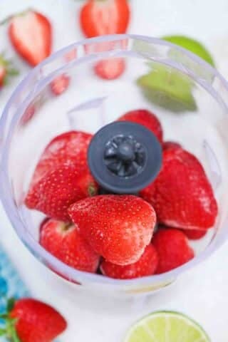 adding frozen strawberries to a blender