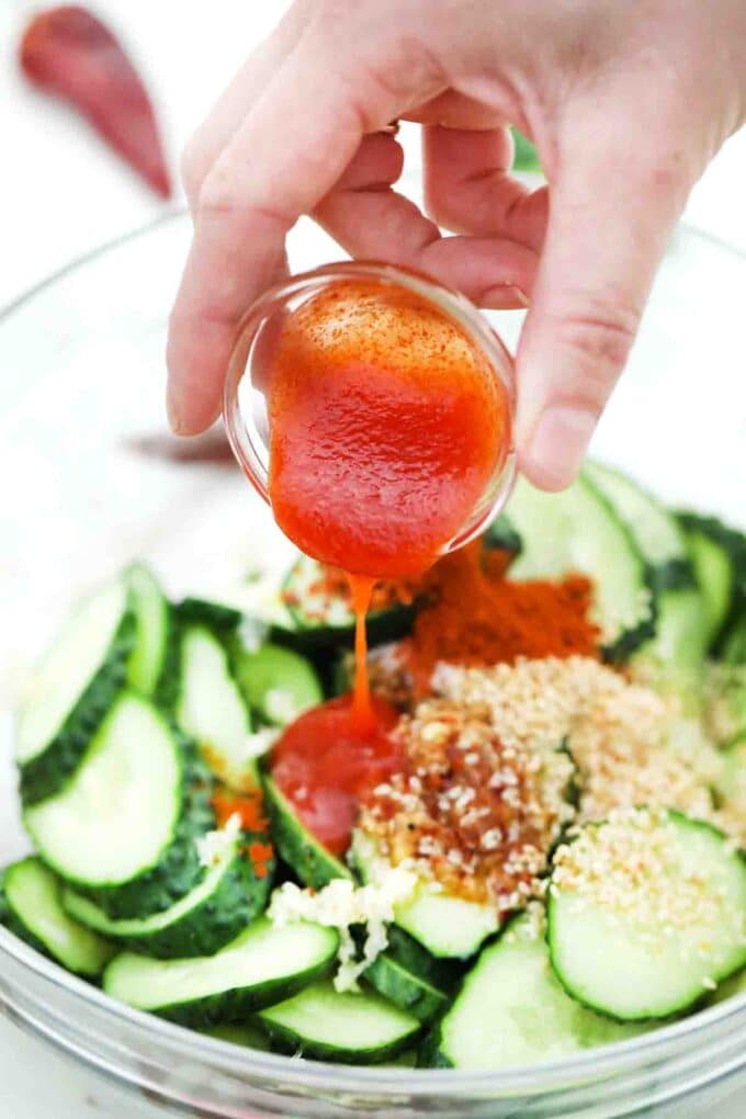 adding spicy sauce to cucumber salad