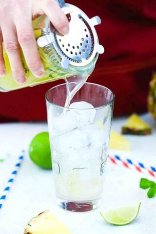 pouring pineapple mojito into a glass