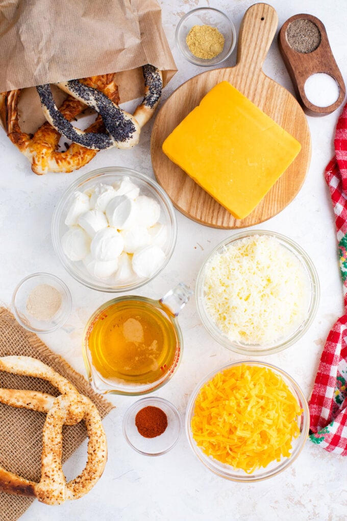 Overhead shot of beer cheese dip ingredients in bowls on a white surface.