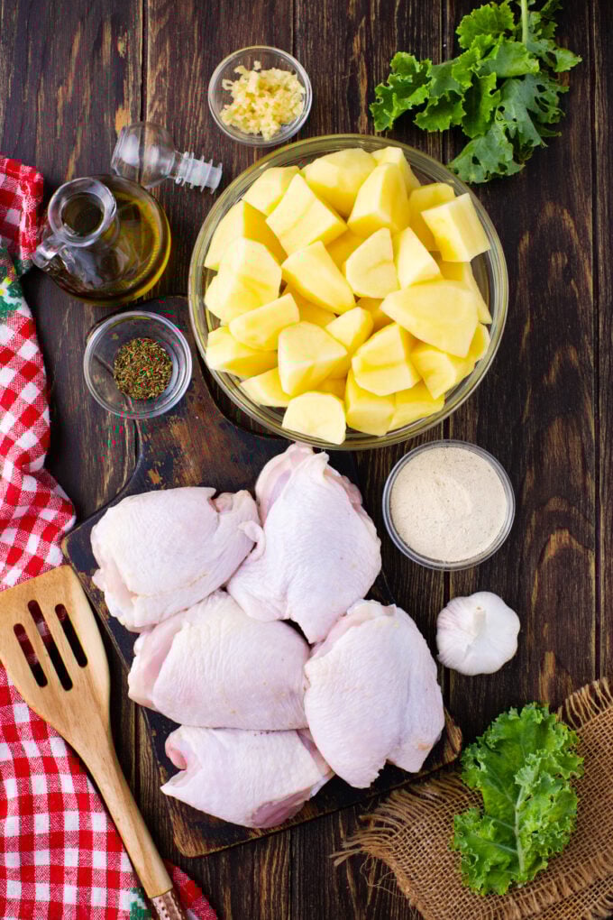 Overhead shot of chicken and potatoes ingredients in bowls on a wooden surface.