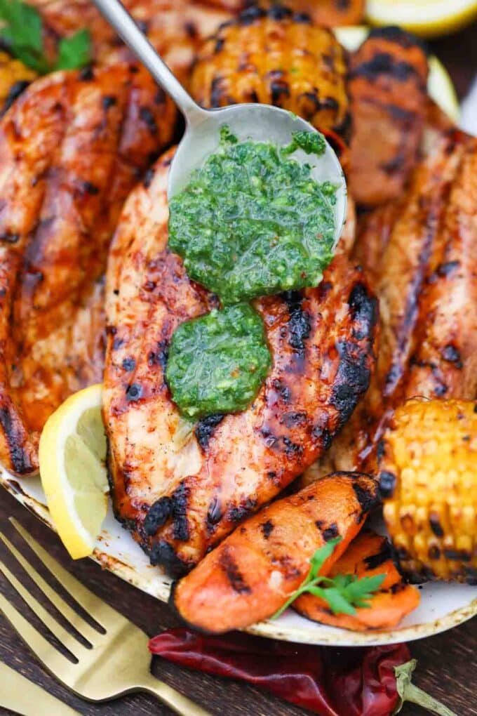 pouring chimichurri sauce over grilled chicken