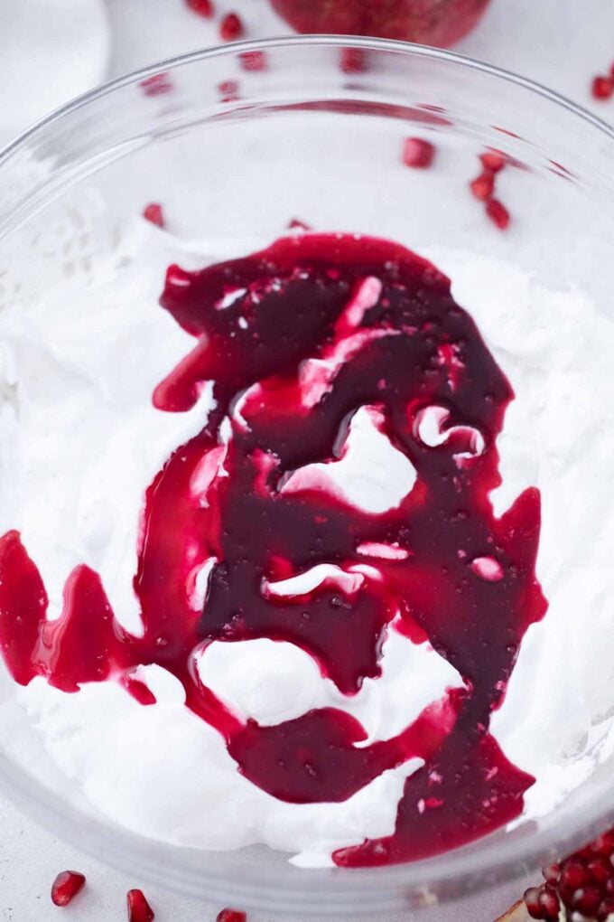 adding pomegranate gelatin mixture to a bowl of whipped cream