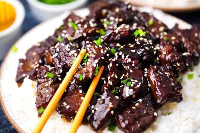 chopsticks holding a piece sticky honey garlic beef on top of rice