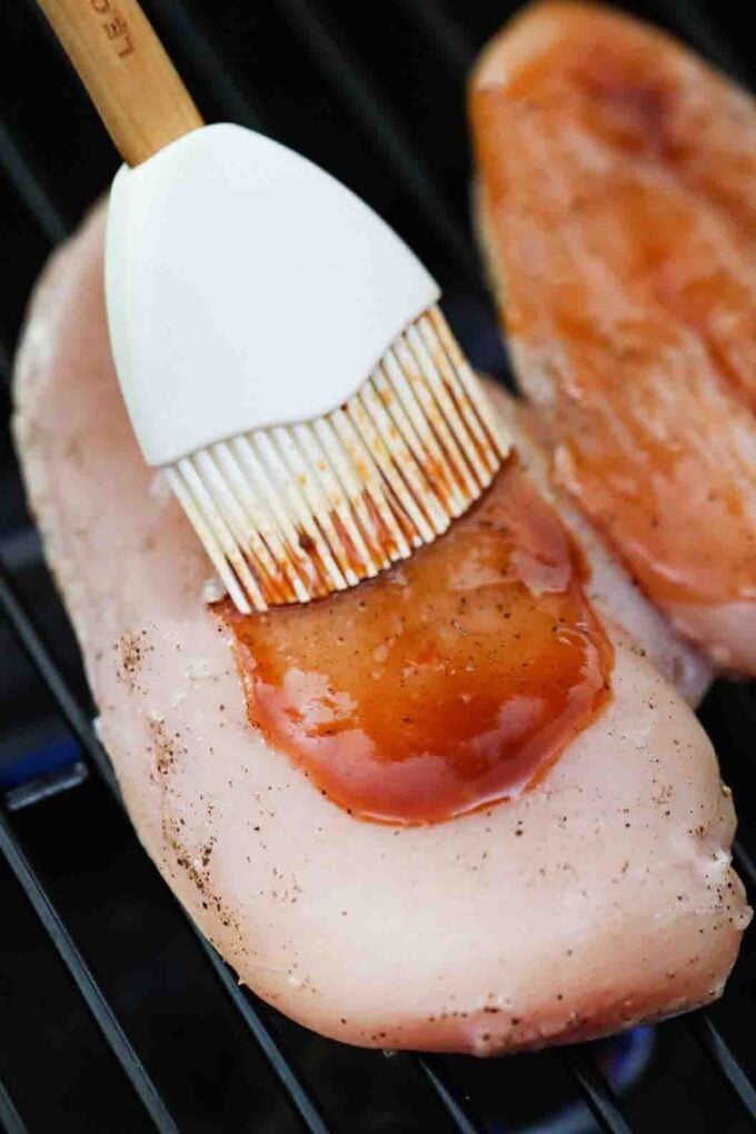smothering chicken breast with bbq sauce on the grill