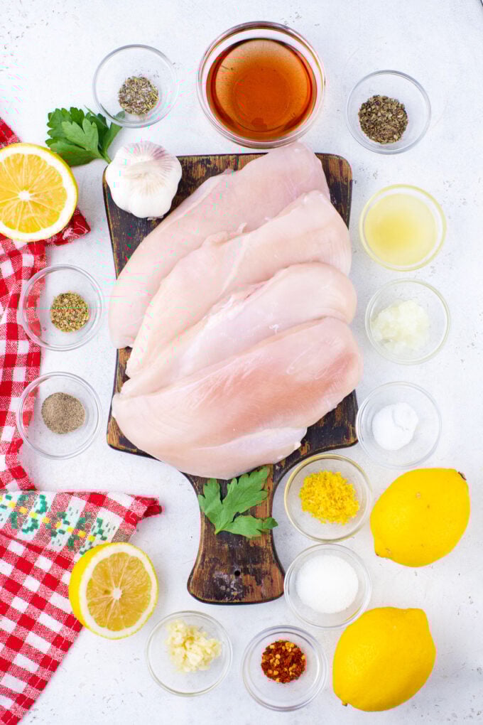 Overhead shot of grilled chicken ingredients in bowls on a white surface.