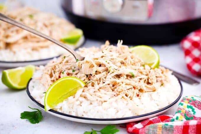 A plate of instant pot shredded chicken over rice served with lime wedges.
