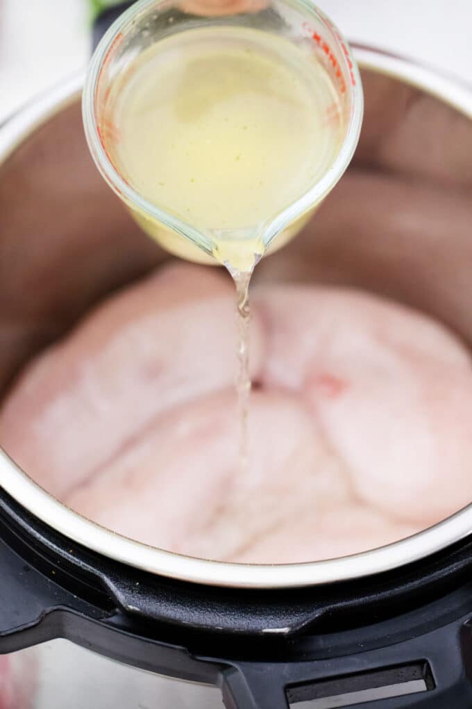 Pouring broth over chicken breasts in an instant pot.